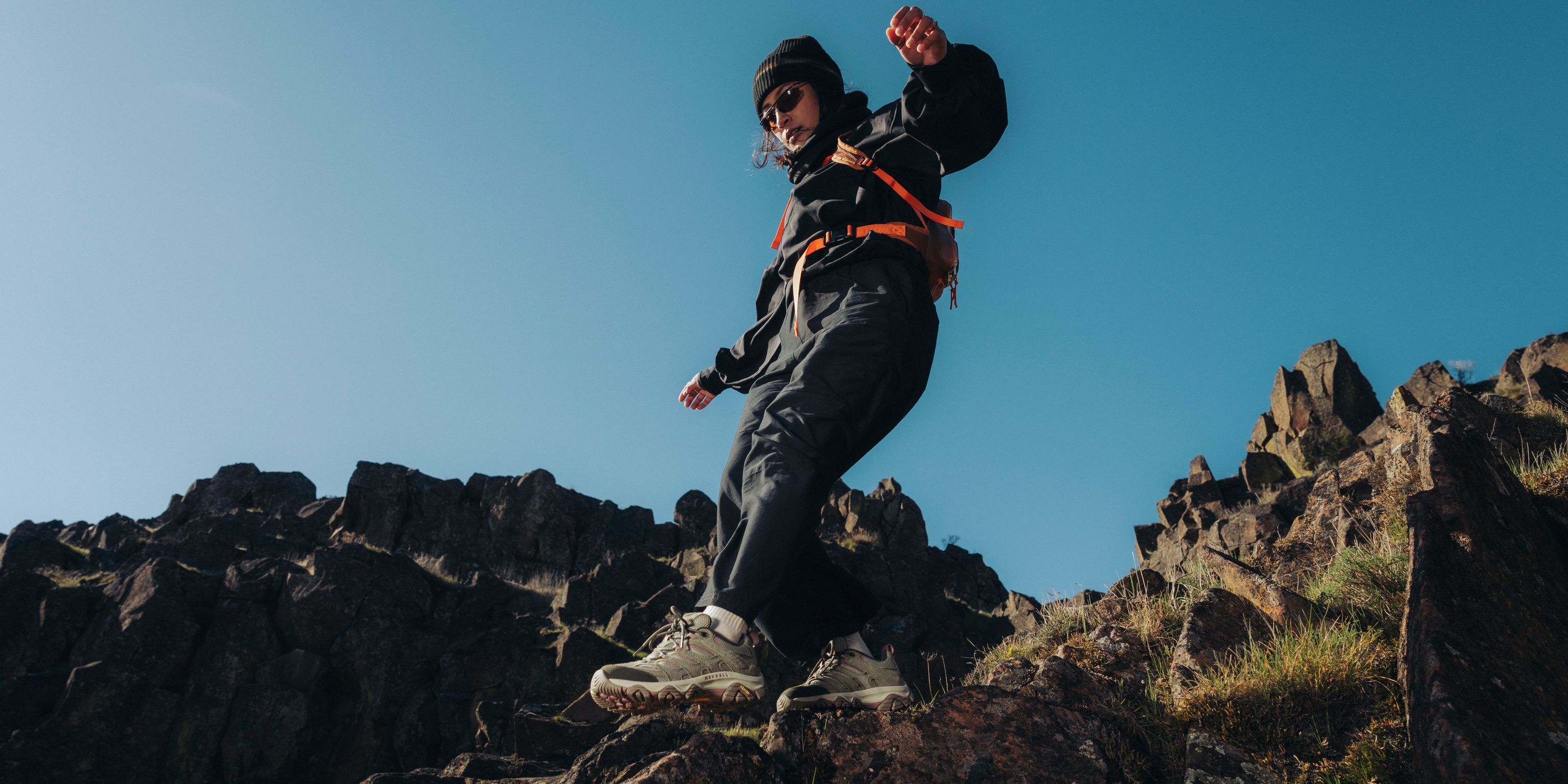 Hiker wearing Merrell hiking shoes on rocky terrain beneath a blue sky